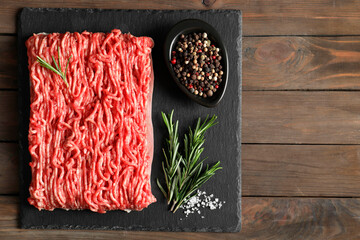 Raw ground meat, spices and rosemary on wooden table, top view. Space for text