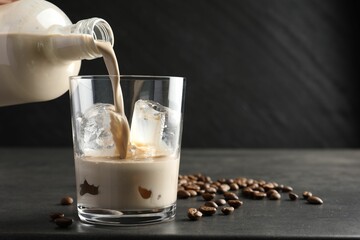 Pouring coffee cream liqueur into glass at grey table, closeup. Space for text
