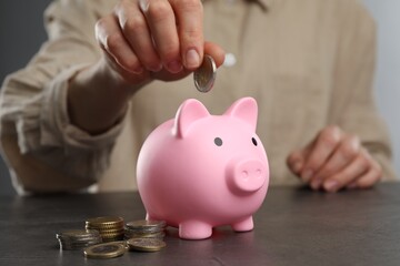 Woman putting coin into pink piggy bank at black table, closeup