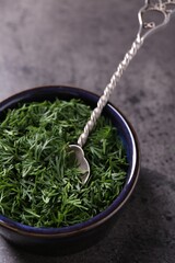 Fresh cut dill in bowl and spoon on grey textured table, closeup