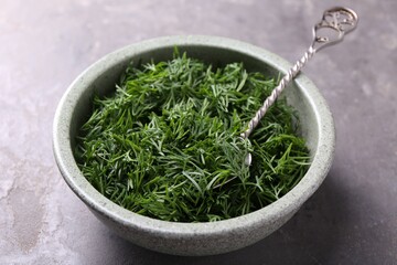 Fresh cut dill and spoon in bowl on grey textured table, closeup
