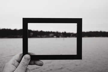 Cropped hand holding a photo frame against the sea