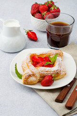 Puff pastry with strawberries, coffee with milk on a light background. Light breakfast, snack.