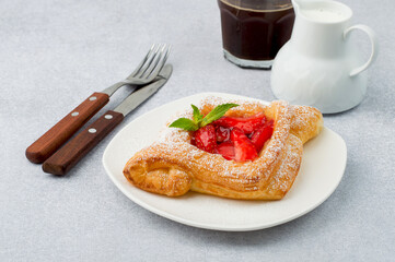 Puff pastry with strawberries, coffee with milk on a light background, horizontal. Light breakfast, snack.