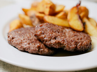 Beef burger and potato wedges on a white plate. Simple plain meal. Dinner with meat product and vegetable.
