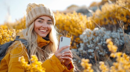 Fototapeta premium A female traveler with a backpack takes a selfie among yellow flowers, wearing a beanie and a warm smile.