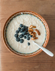 Healthy breakfast meal: Oatmeal porridge with white rise, vaccinium corymbosum berries and pecan nuts in a bowl plate with spoon