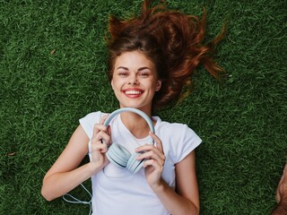 Woman in headphones portrait lying on the grass and listening to music looking at the camera smile...