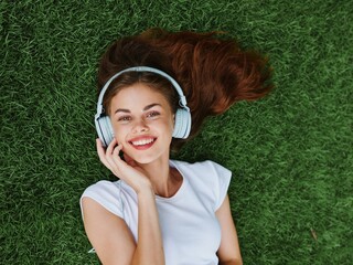 Beautiful woman wearing headphones listening to music lying on the grass on the lawn in the park in...