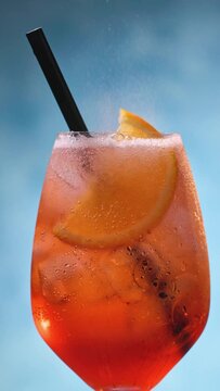 Glass of apperol spritz cocktail with orange slice and straw on blue background. Closeup of summer drink, zoom in