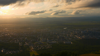 Top view of city in green valley with sun on horizon. Clip. Beautiful landscape of sunny green valley with town on summer day. Bright sun shines down on valley with town