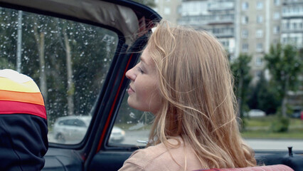 Young couple in countryside area sitting together in a car. Stock. Red flag on a back seat, retro car in a village.