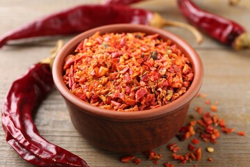 Aromatic spice. Red chili pepper flakes in bowl and pods on wooden table, closeup