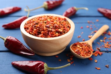 Chili pepper flakes and pods on blue wooden table, closeup