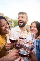 Vertical. Cheerful international friends toasting glasses of red wine together laughing at terrace...