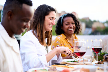 Side view of smiling Caucasian woman holding fork and knife eating food sitting at table with...