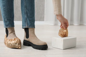 Woman wearing shoe covers onto her boots indoors, closeup
