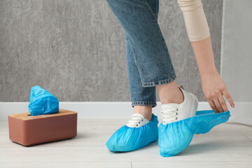 Woman wearing blue shoe covers onto her sneakers indoors, closeup