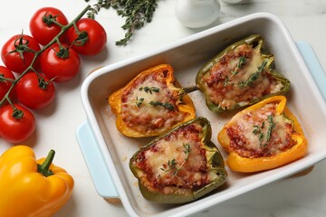 Tasty stuffed peppers in dish and ingredients on white table, flat lay