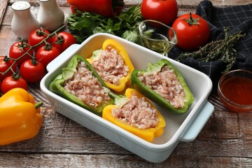 Raw stuffed peppers in dish and ingredients on wooden table