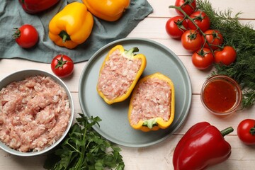 Raw stuffed peppers with ground meat and ingredients on light wooden table, flat lay