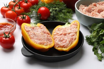 Raw stuffed peppers with ground meat and ingredients on white tiled table