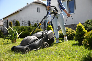 Woman cutting green grass with lawn mower in garden, closeup