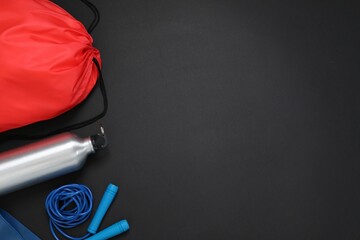 Red drawstring bag, skipping rope and thermo bottle on black background, flat lay. Space for text