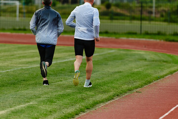 An inspiring and active elderly couple showcase their dedication to fitness as they running together on a lush green field, captured in a close-up shot of their legs in motion.
