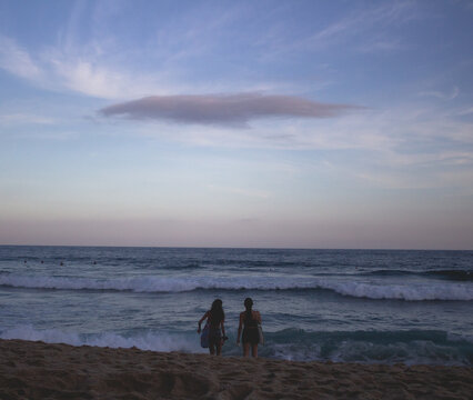 Duas garotas olhando para o mar em um lindo entardecer de c&eacute;u azul e roxo