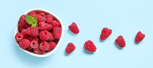 Bowl with fresh raspberries and mint on blue background