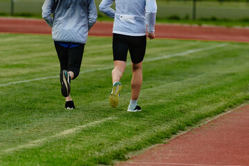 Fototapeta premium An inspiring and active elderly couple showcase their dedication to fitness as they running together on a lush green field, captured in a close-up shot of their legs in motion.