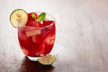 Decorative tropical cold beverage ' Watermelon Vodka Cosmo'. Garnished with Lemon wedge and Mint leaves, on a wooden table.