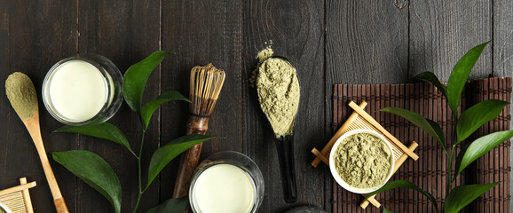 Composition with cups of fresh matcha tea, powder and accessories on dark wooden background