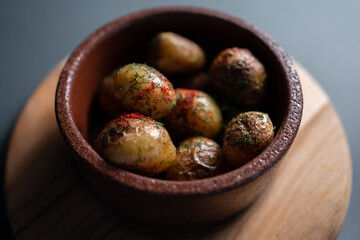 roasted potatoes with herbs and spice in clay bowl on black background, closeup