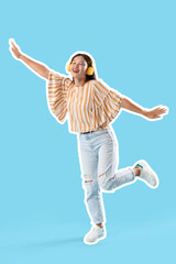 Young Asian woman with painted face in headphones dancing on blue background