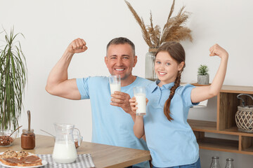 Little girl with her father drinking milk and showing muscles in living room