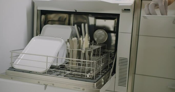 Woman preparing instruments for beauty procedures, doing disinfection and sterilization of manicure tools using automatic disinfector washer and autoclave in special room.