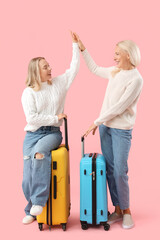 Happy young beautiful woman and her mother with suitcases giving each other high-five on pink...