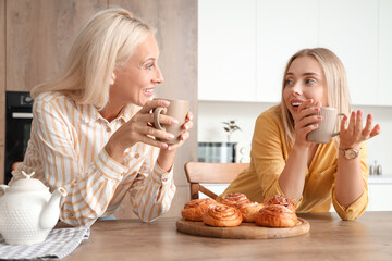 Beautiful young woman and her mother drinking tea with tasty buns in kitchen