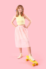 Young woman with skateboard on pink background