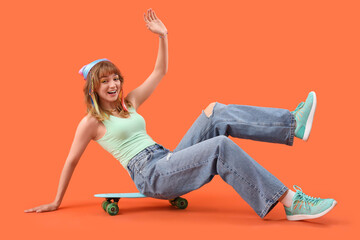 Young woman with skateboard sitting on orange background