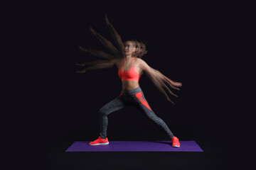 Young female trainer exercising in motion on black background