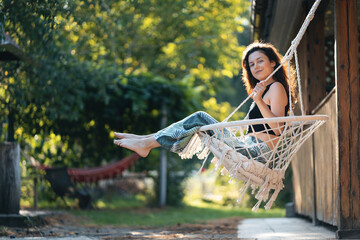 happy young female riding on macrame swing chair near country house outdoors