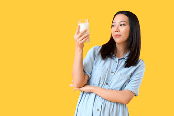 Young Asian woman with glass of milk on yellow background