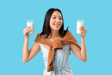 Young Asian woman with glasses of milk on blue background