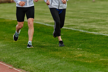 Fototapeta premium An inspiring and active elderly couple showcase their dedication to fitness as they running together on a lush green field, captured in a close-up shot of their legs in motion.