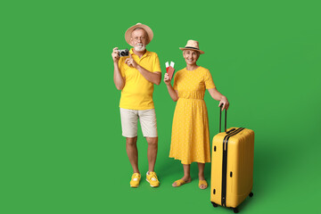 Mature couple of travelers with passports, photo camera and suitcase on green background
