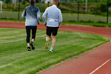 An inspiring and active elderly couple showcase their dedication to fitness as they running together on a lush green field, captured in a close-up shot of their legs in motion.