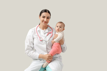 Female pediatrician with little baby sitting on light background